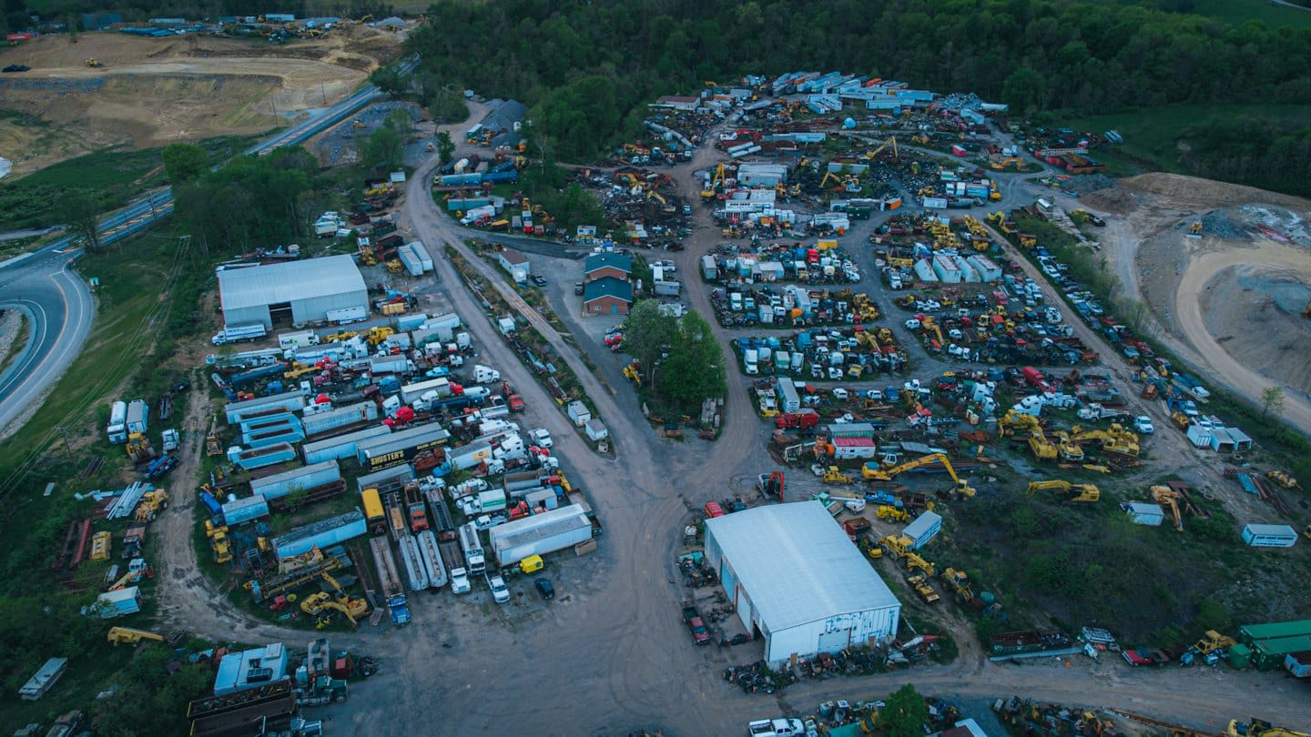 Endüstriyel bir hurdalıkta park edilmiş ekskavatör ve kamyon sıraları.