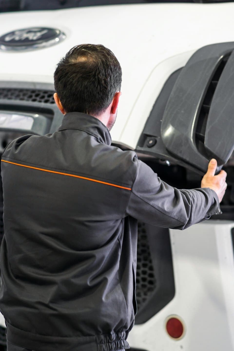 Gri bir paneli tutan tamirci, büyük bir aracın motor bölümünü inceliyor.